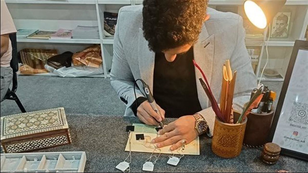 «ذكرى من معرض الكتاب».. خطاط يمني يجذب الزوار لنقش أسمائهم بالخط العربي